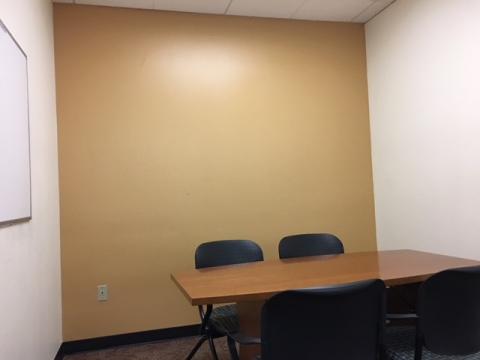 Small meeting room with table, white board mounted on wall, and seating for four