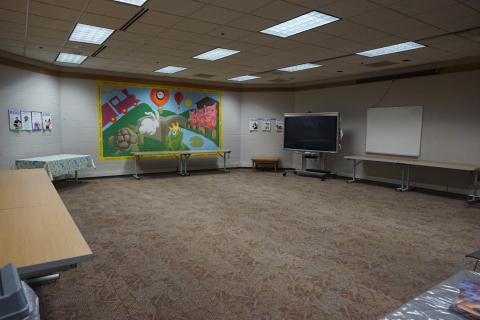 Large open room with carpet, tables lining the walls, and a colorful mural
