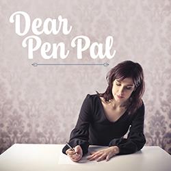 A woman in a dark dress writing a letter on a white tabletop with an out of focus floral print wallpaper background