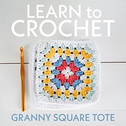 A granny square in blues, yellows, reds, and white with a gold crochet hook to the left seen from above