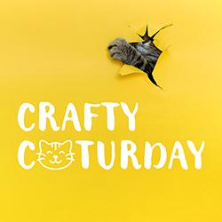 A gray tabby cat has torn a hole in yellow paper and poked a paw through