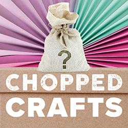 A burlap mystery bag of craft supplies on top of a cardboard box with a multicolored paper fan behind.