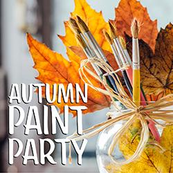 A glass vase filled with paint brushes and colorful autumn leaves.