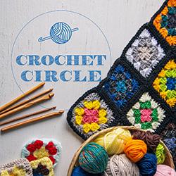 A basket of colorful balls of yarn, crochet hooks, and a multicolored granny square blanket seen from above on a gray tabletop.