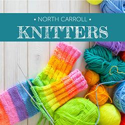 Colorful yarns and knitting needles on a gray wooden tabletop.