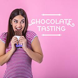 A woman in a pink and white striped shirt nibbling a chocolate bar in front of a pink background