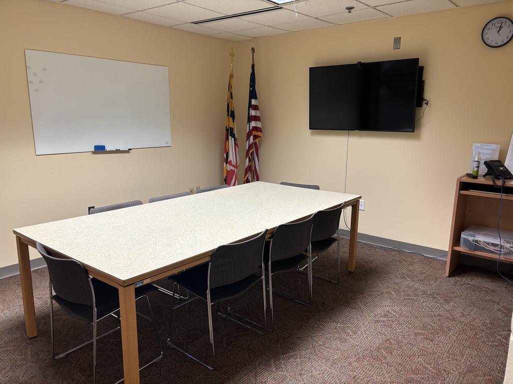 Rectangular table with chairs, large computer monitor and whiteboard.