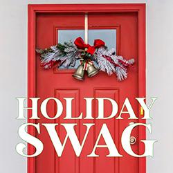 A red door decorated with a swag of pine boughs, silver bells, and a red bow.